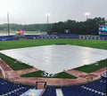 Baseball field with a tarp over it, surrounded by stadium seating and advertisements.